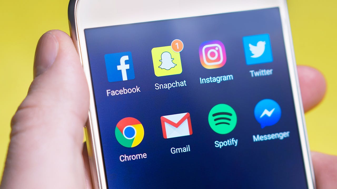 A person's hand holding a smartphone displaying social media and communication apps.